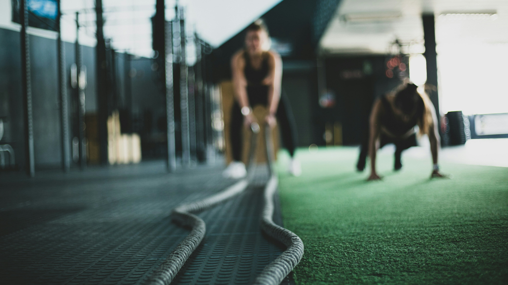 One woman working out at Mojo Fitness Littleton doing a plank and another woman battling ropes