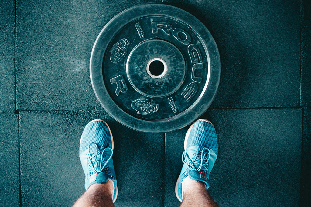 Photo of man standing in Mojo Fitness Littleton with his blue tennis shoes on ready to workout with a barbell weight