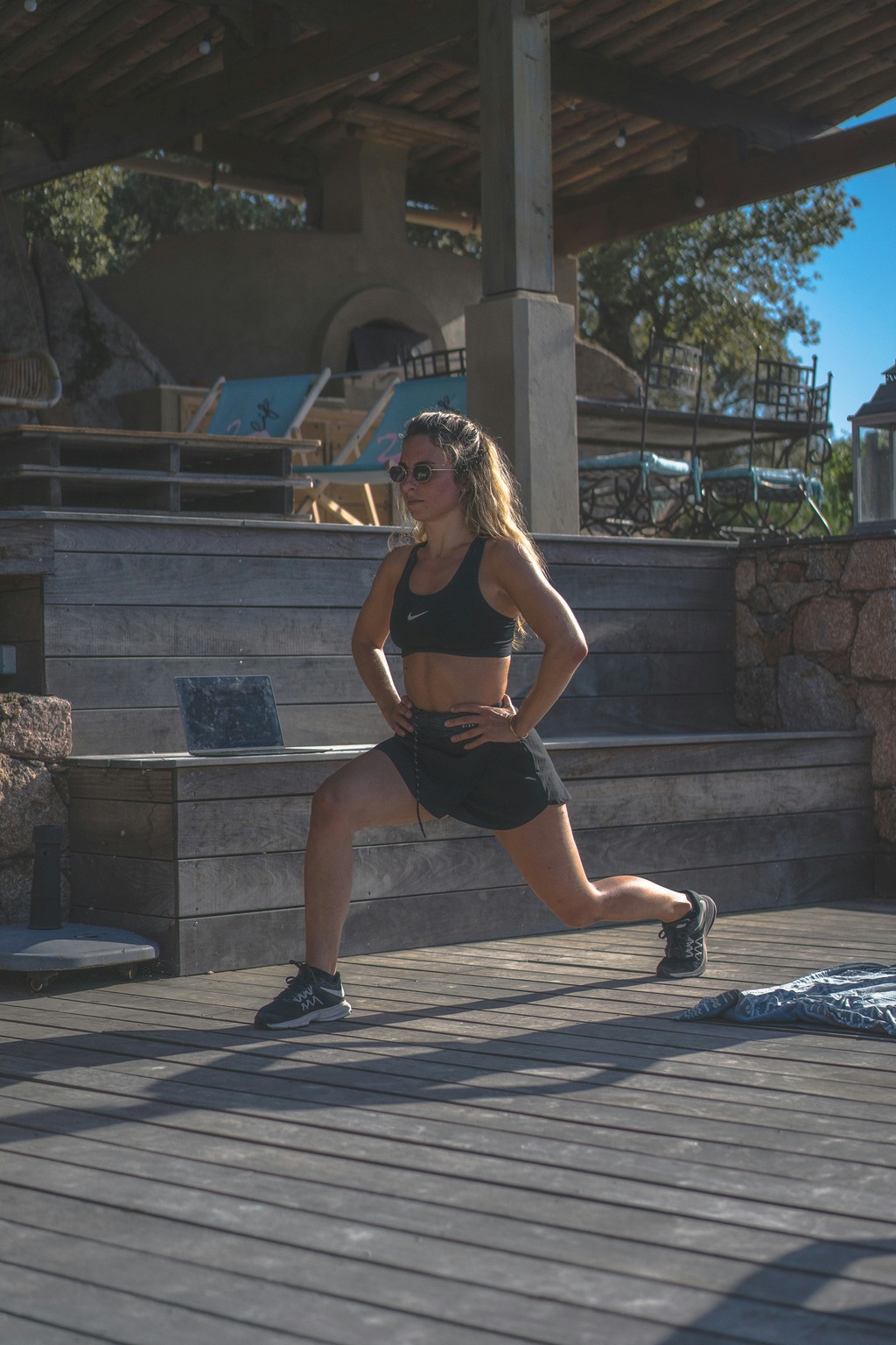 Young woman performing a lunge exercise outdoors on a wooden deck.