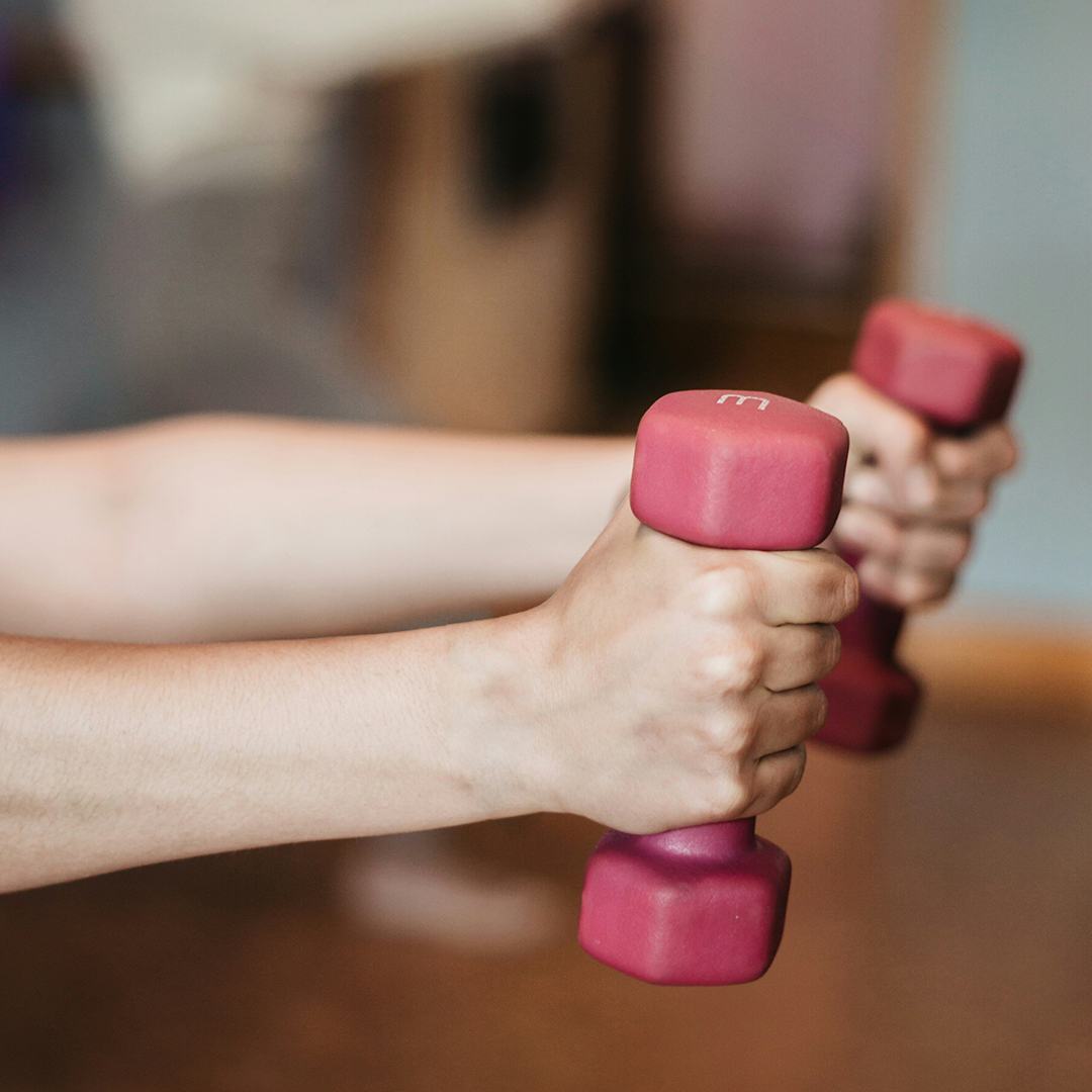 Close-up view of a person's hands lifting pink dumbbells, focusing on muscle building exercises.