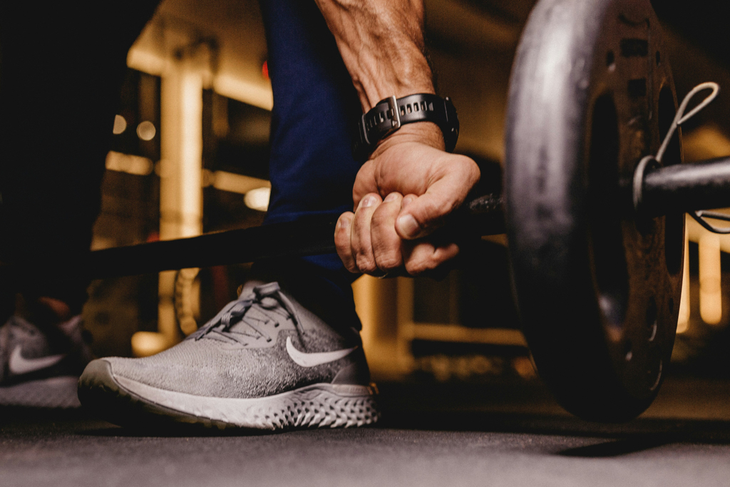 Close-up of a man's hands gripping a weightlifting barbell at Mojo Fitness Littleton, emphasizing strength training and personal fitness.