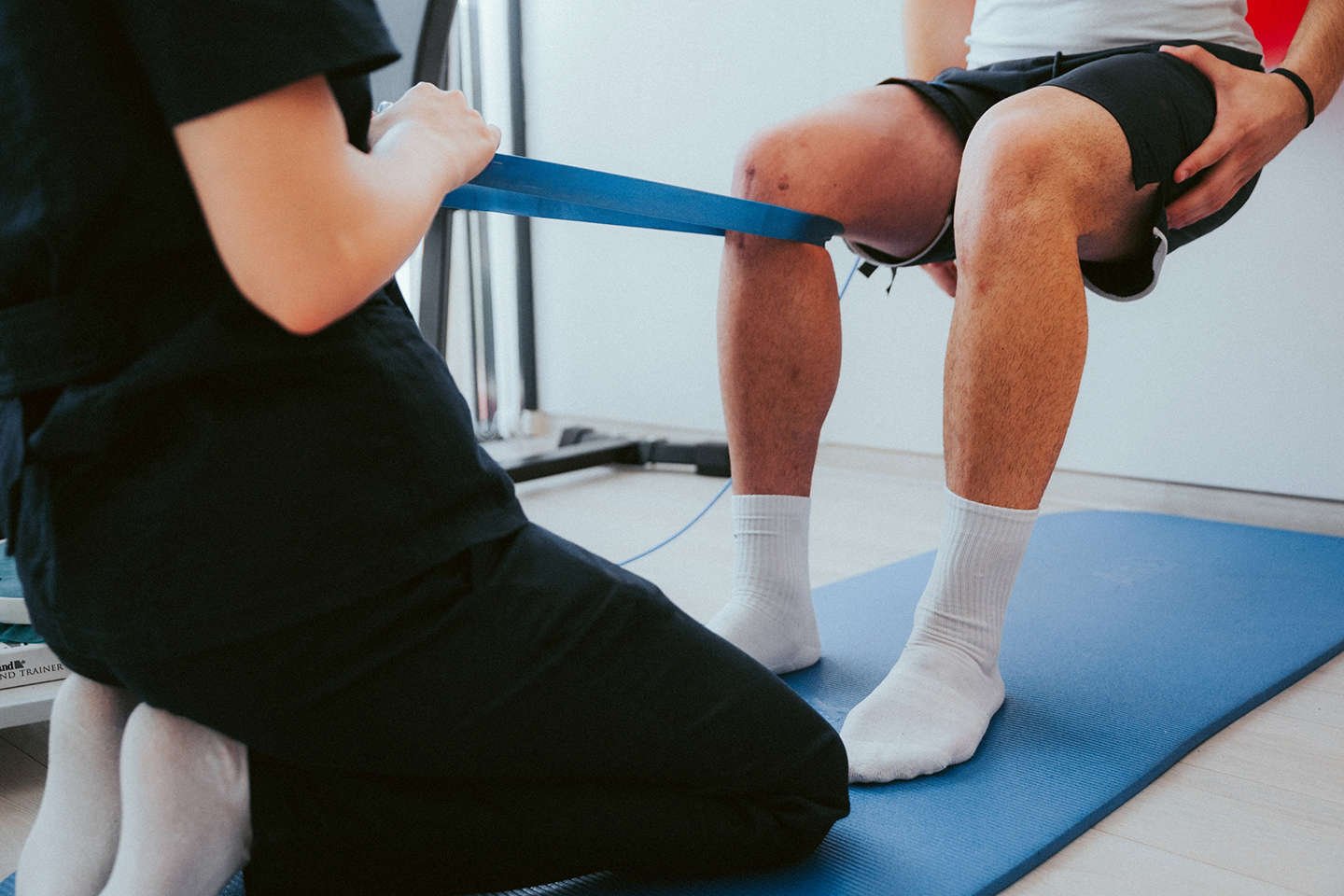 Close-up of a therapist assisting a patient with a resistance band exercise for knee rehabilitation, emphasizing expert guidance in injury recovery.