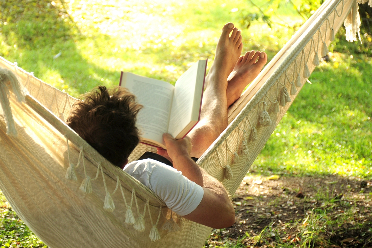 Person relaxing in a hammock while reading a book, set in a sunny outdoor environment. The scene highlights the importance of rest and recovery in a fitness plan, emphasizing the need for downtime and relaxation to support overall well-being and physical health.