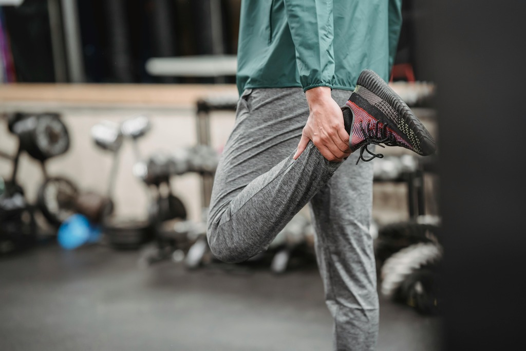 Man stretching in a gym, holding his foot to his buttock to stretch his quadriceps at Mojo Fitness Littleton.