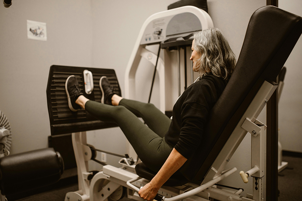 A senior woman with gray hair performs a leg press, showcasing the importance of strength training for weight loss and overall health.